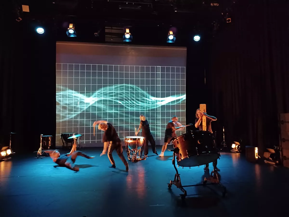 Dove en horende musici repeteren samen. Op een groot scherm zijn visuele weergaven van het geluid dat ze maken te zien.