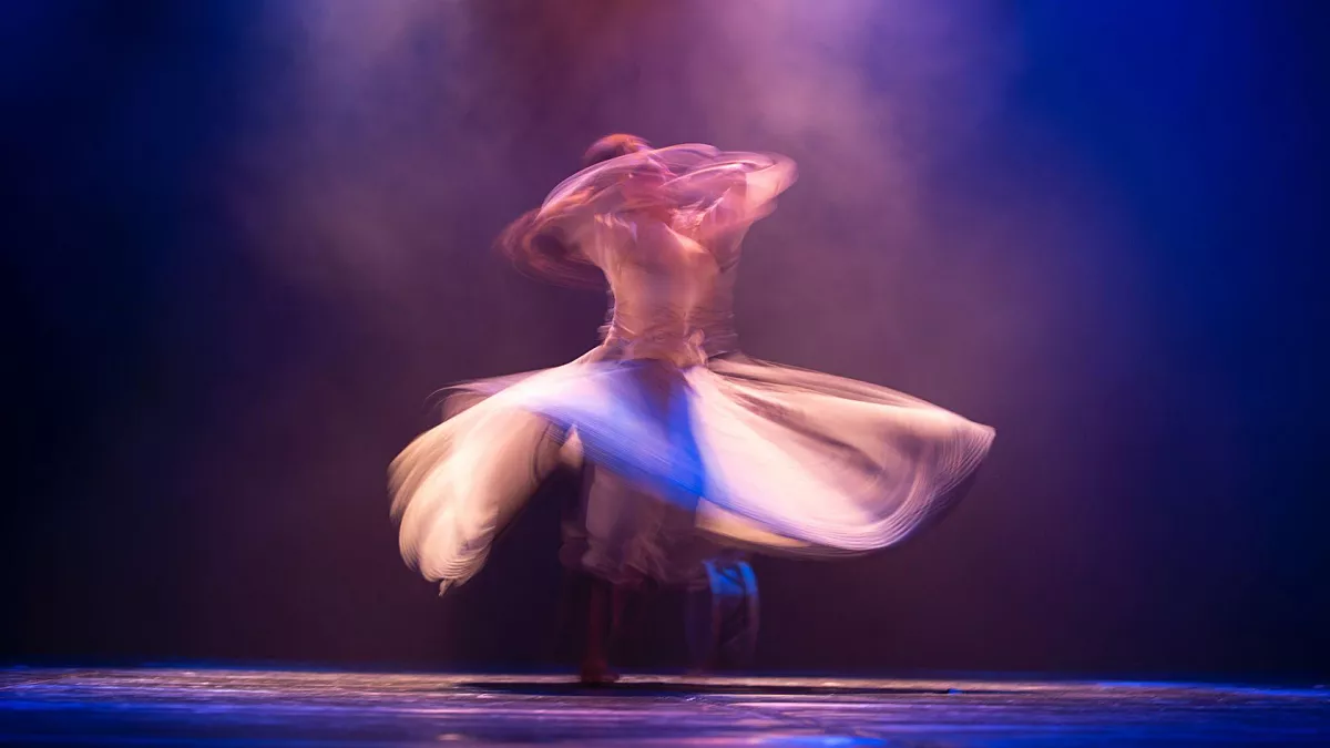Danser maakt pirouettes in een jurk die rondom het lichaam zwiert. Foto is gemaakt met multiple exposure effect, hierdoor lijken er meerdere bewegingen gevat in één frame.