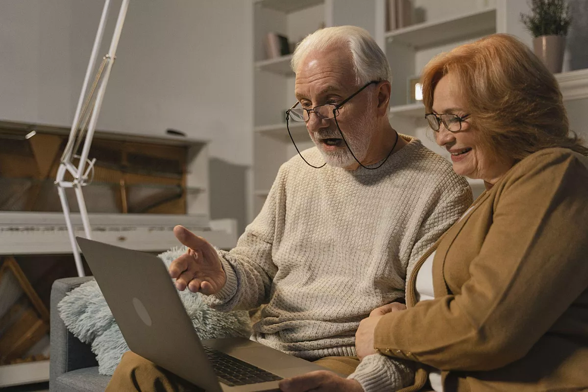 Two elderly are looking amused at a laptop.