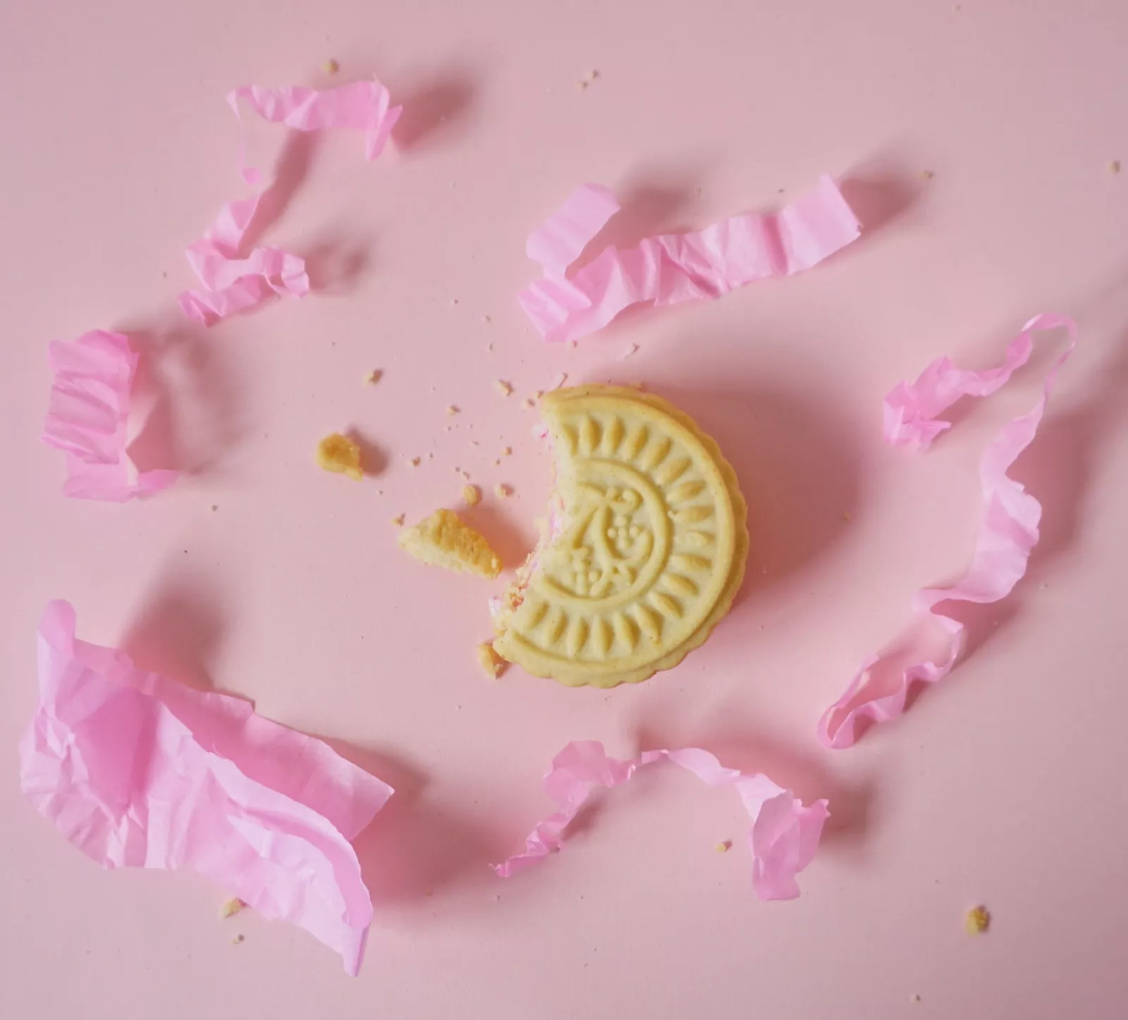 Afgebroken koekje op een roze achtergrond met gescheurde roze verpakking ernaast.