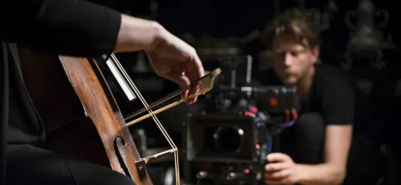 Een man met filmcamera die cellist filmt