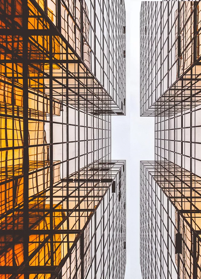 Doorkijkje tussen twee hoge gebouwen met oranje en glas. Perspectief is vanaf de grond omhoog kijkend.