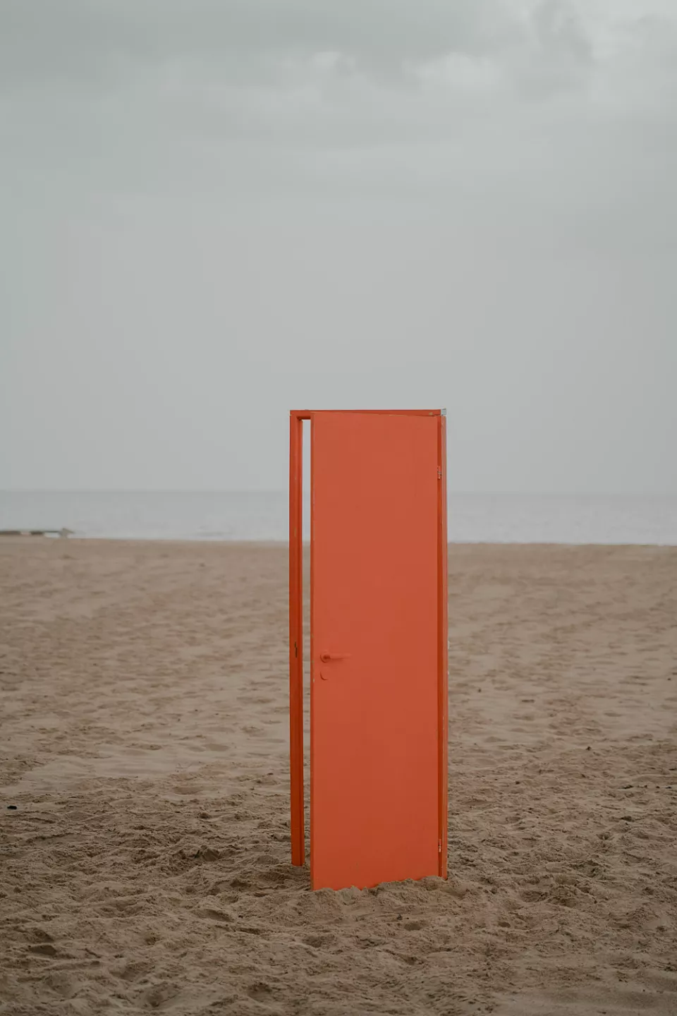 Orange door standing upright on the beach. The door is ajar.