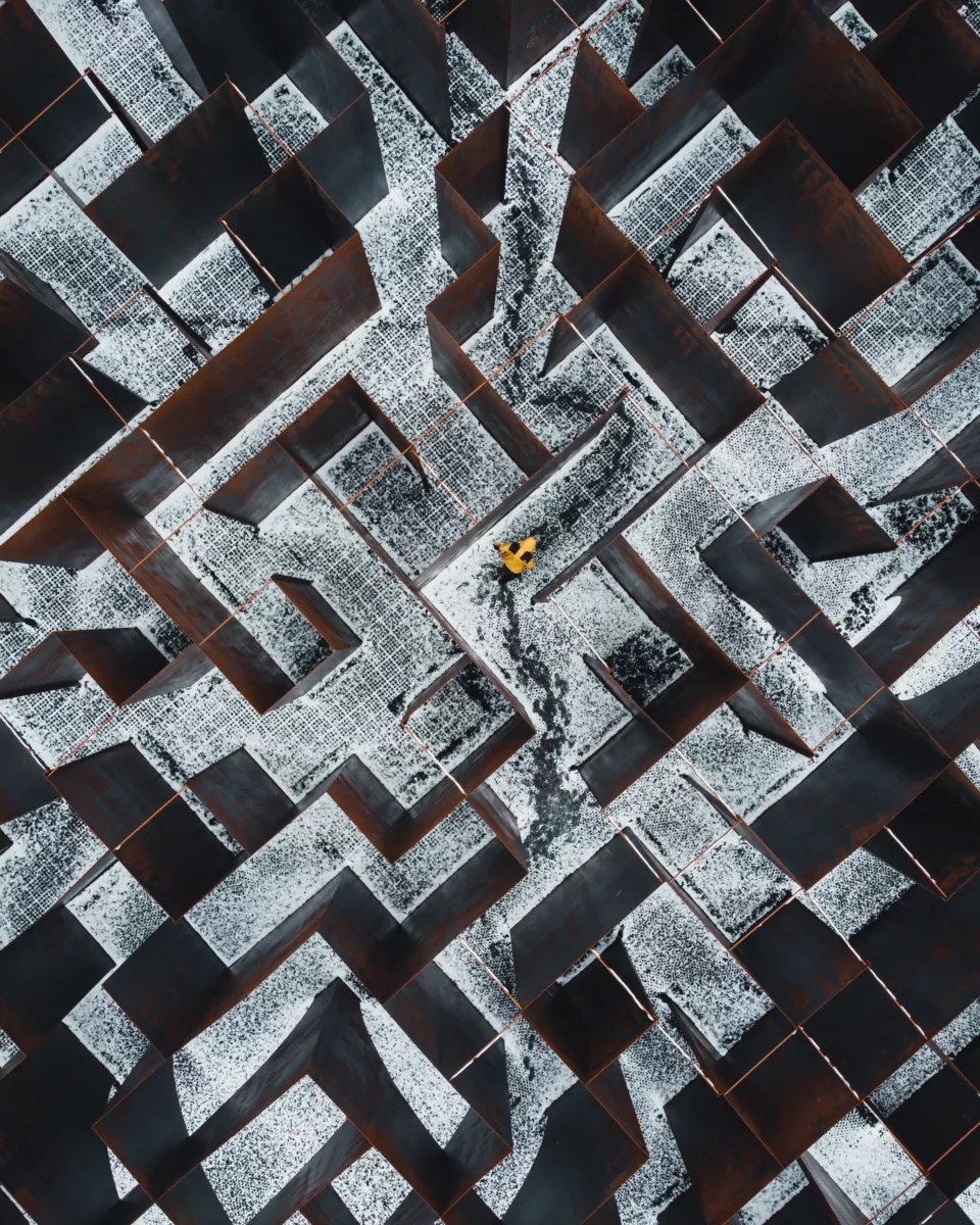 Maze seen from above. Through the maze walks someone with a bright yellow coat.